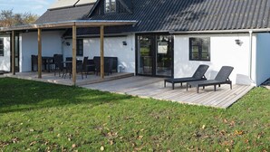 A modern house with a covered patio, a chimney, and a deck with outdoor furniture. - 8 Person Holiday Home in Sakskobing (Sakskobing)