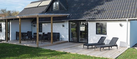 Una casa moderna con un porche cubierto, una chimenea y una terraza con mobiliario exterior.