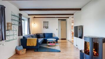 Una sala de estar con un sofá azul, un televisor, una chimenea de leña y una ventana con cortinas.