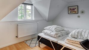 A bedroom with a sloped ceiling, a window with blinds, a radiator, a bed with patterned bedding, and wall decorations. - 8 Person Holiday Home in Sakskobing (Sakskobing)