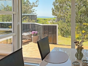 A modern outdoor seating area with a view of the sea, a wooden deck, and a wicker basket with flowers. - 7 Person Holiday Home in Logstor (Logstor)