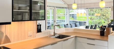 A modern kitchen with a built-in dishwasher, a sink, and a dining area with a view of the outdoors.