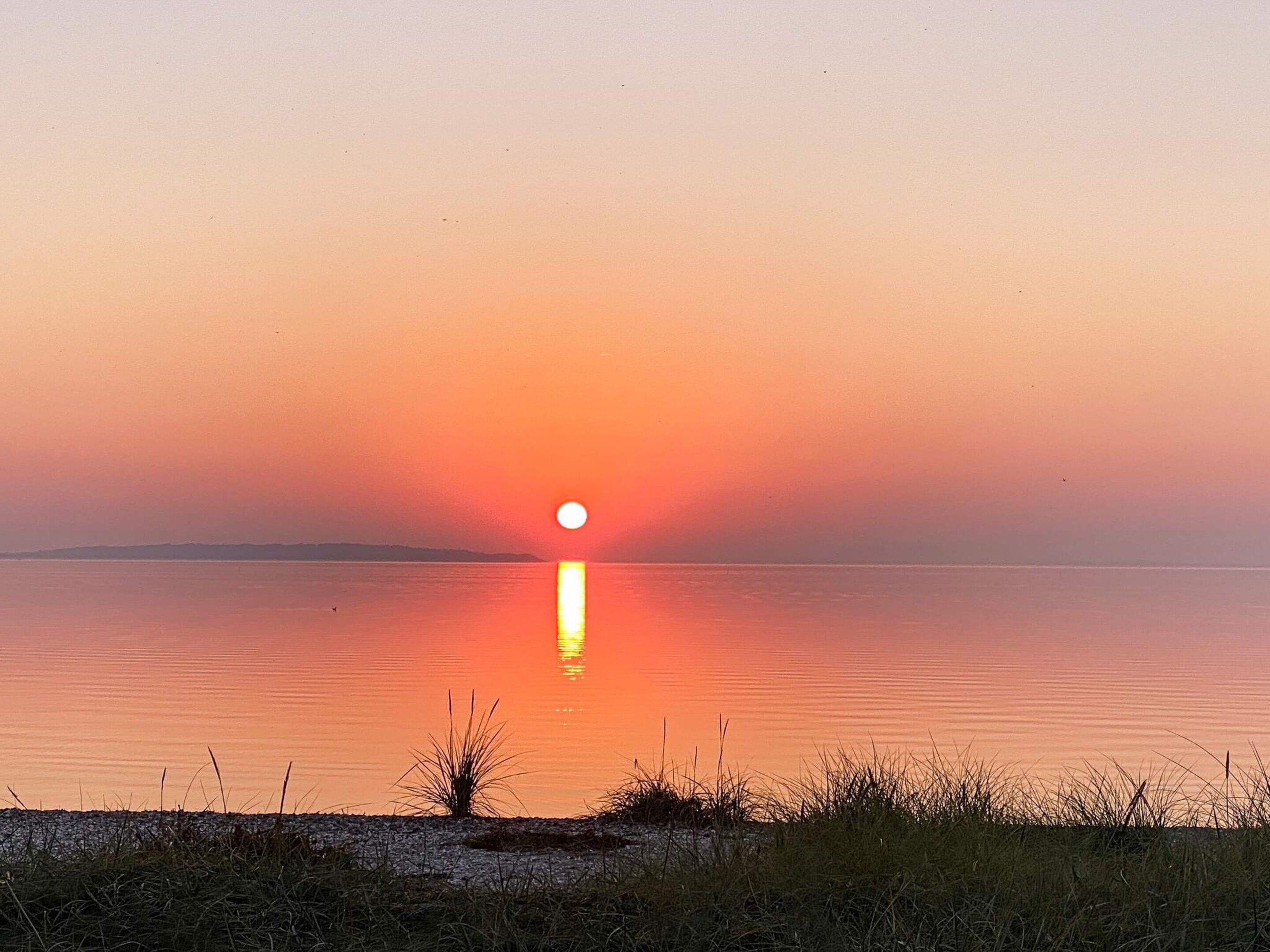 A sunset over a calm body of water with a distant shoreline.
