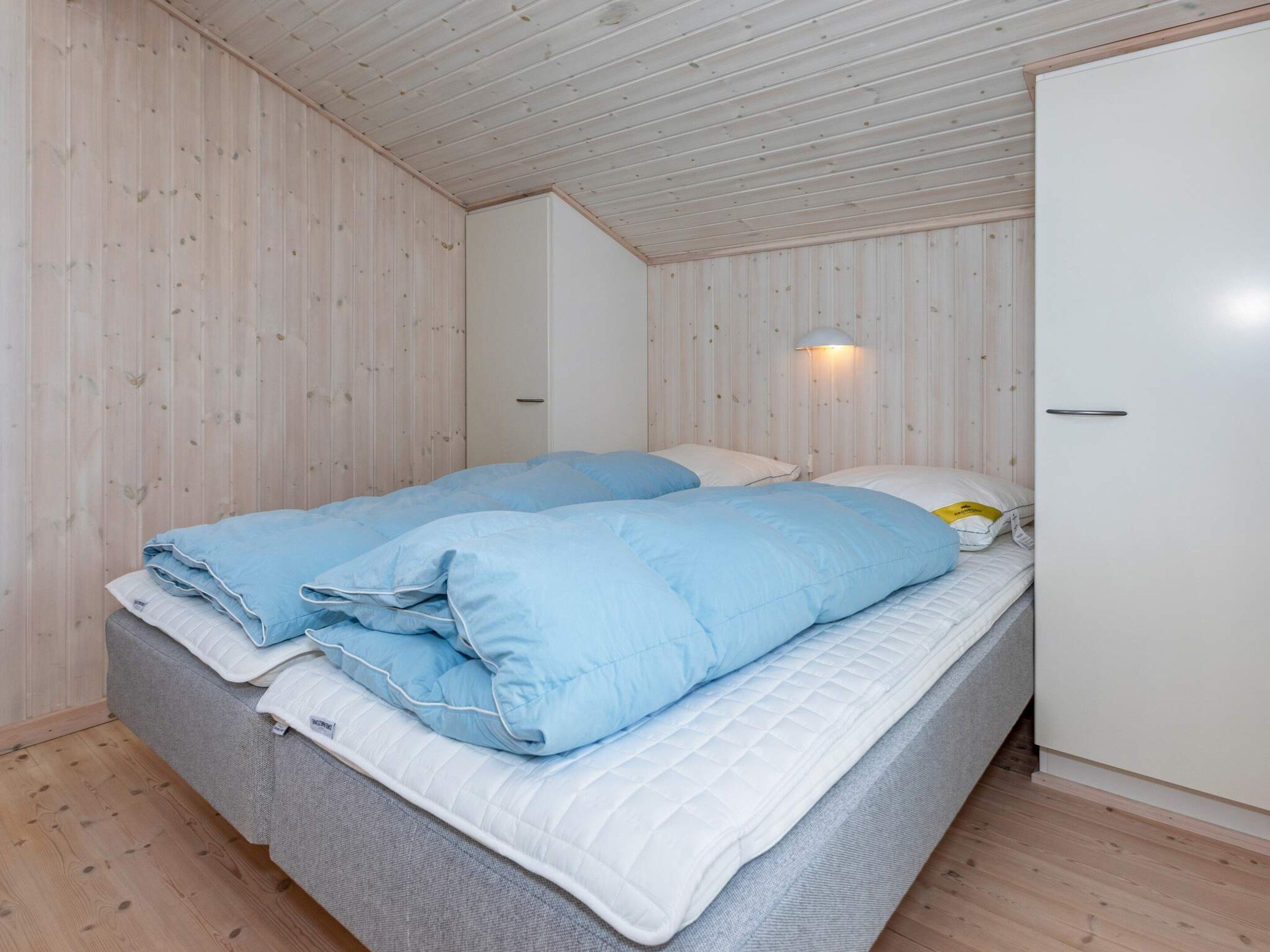 A single bed with blue bedding and a white headboard in a room with wooden walls and a sloped ceiling.