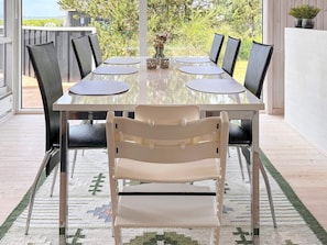 A dining table with six chairs, a glass top, and a view of greenery outside. - 7 Person Holiday Home in Logstor (Logstor)