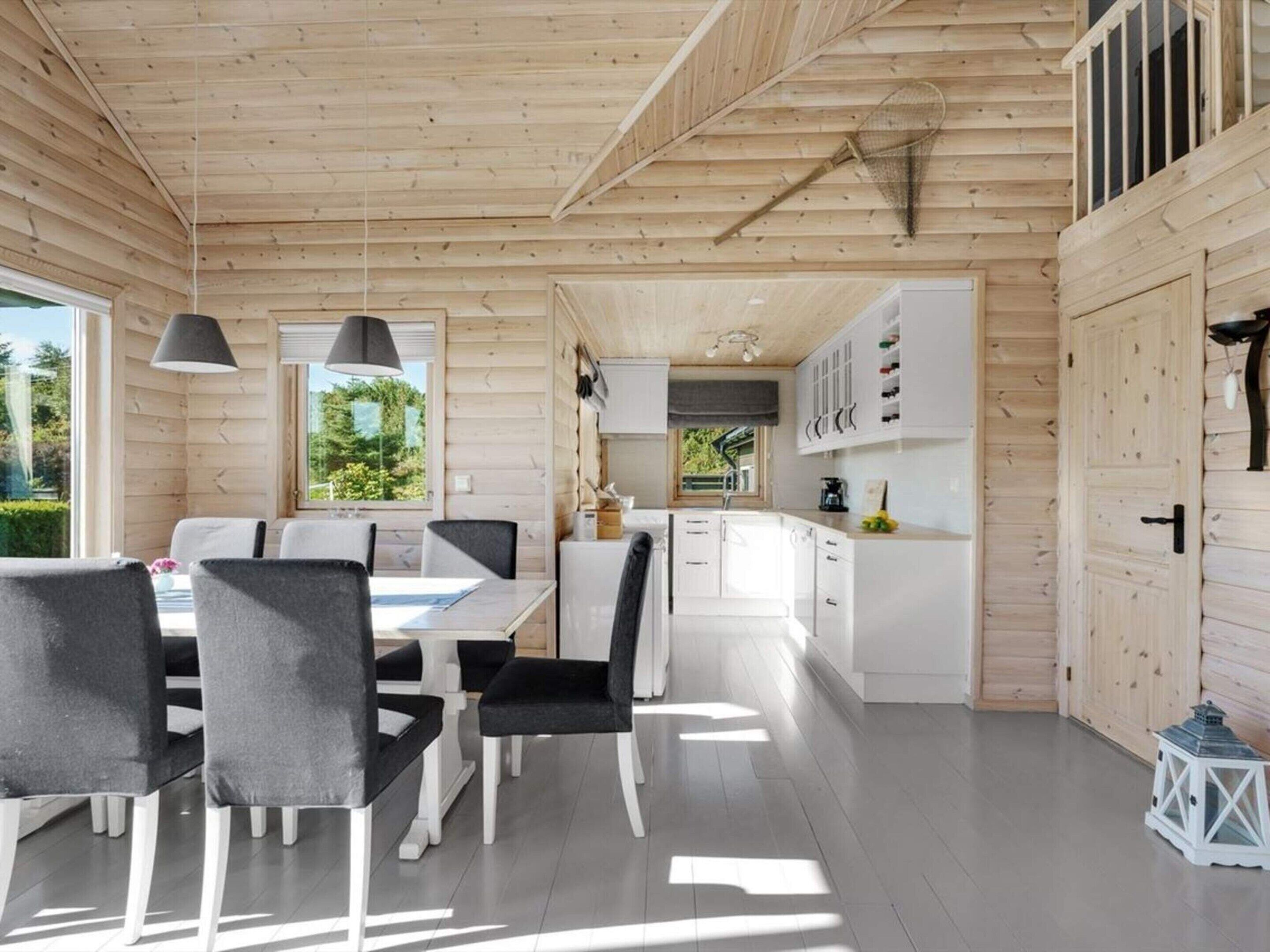 A modern log cabin interior with a dining area, kitchen, and white cabinetry.