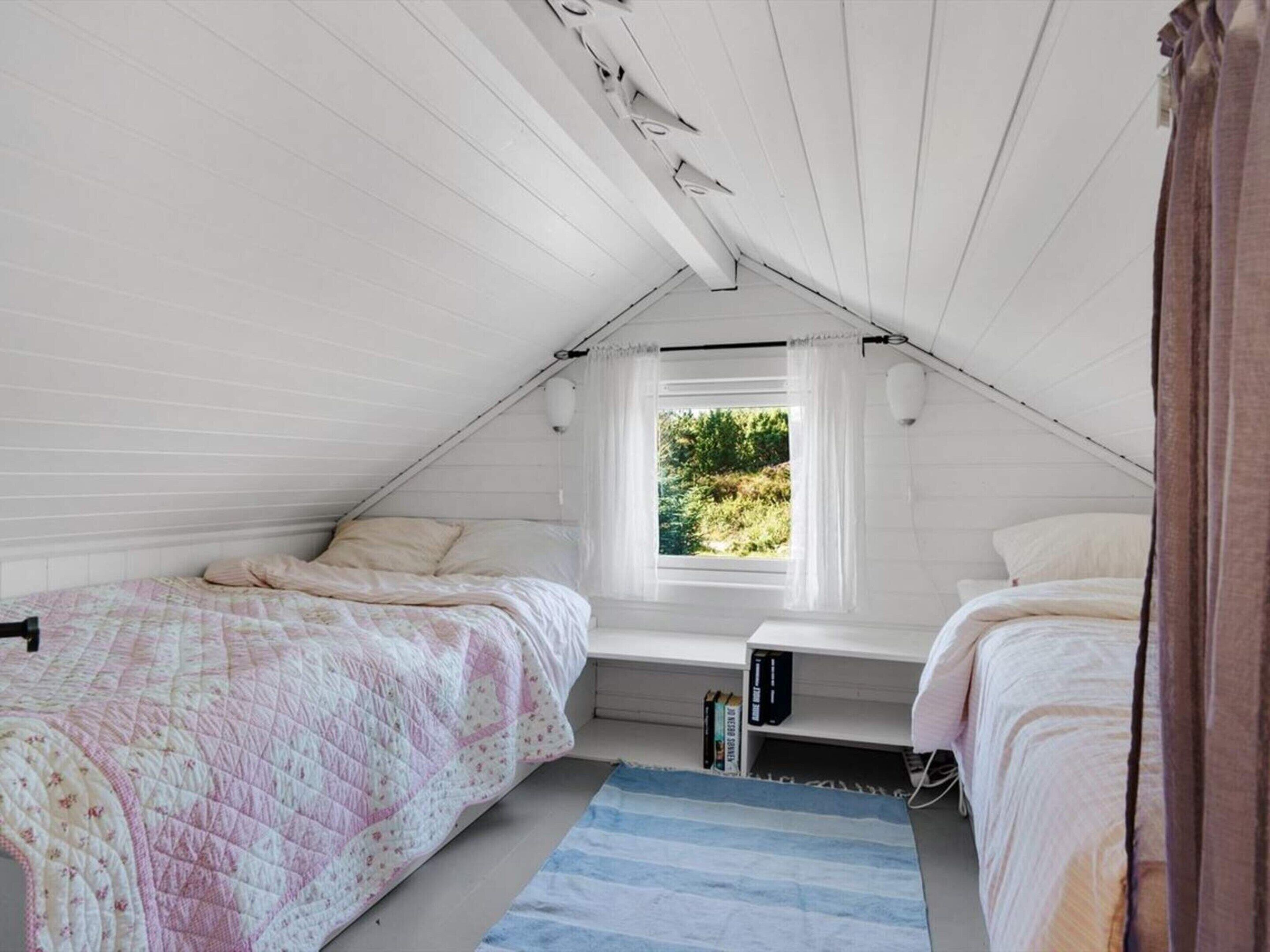 Un dormitorio en ático pequeño con dos camas, una ventana que da a zonas verdes y un techo inclinado.