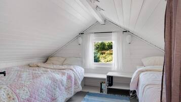 Un dormitorio en ático pequeño con dos camas, una ventana que da a zonas verdes y un techo inclinado.
