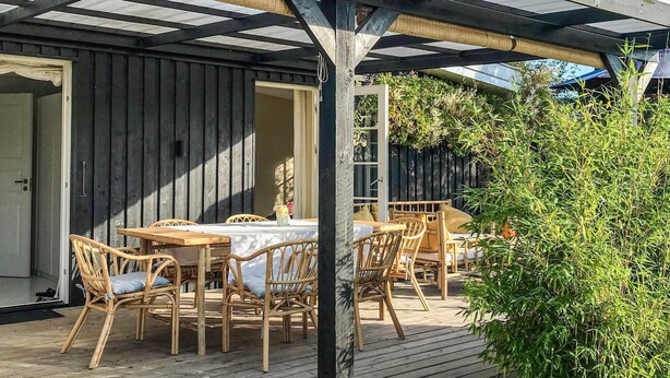 An outdoor dining area with wooden tables and chairs, a pergola overhead, and a wooden deck. - 6 Person Holiday Home in Gilleleje (Gilleleje)