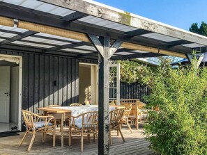 An outdoor dining area with wooden tables and chairs, a pergola overhead, and a wooden deck. - 6 Person Holiday Home in Gilleleje (Gilleleje)