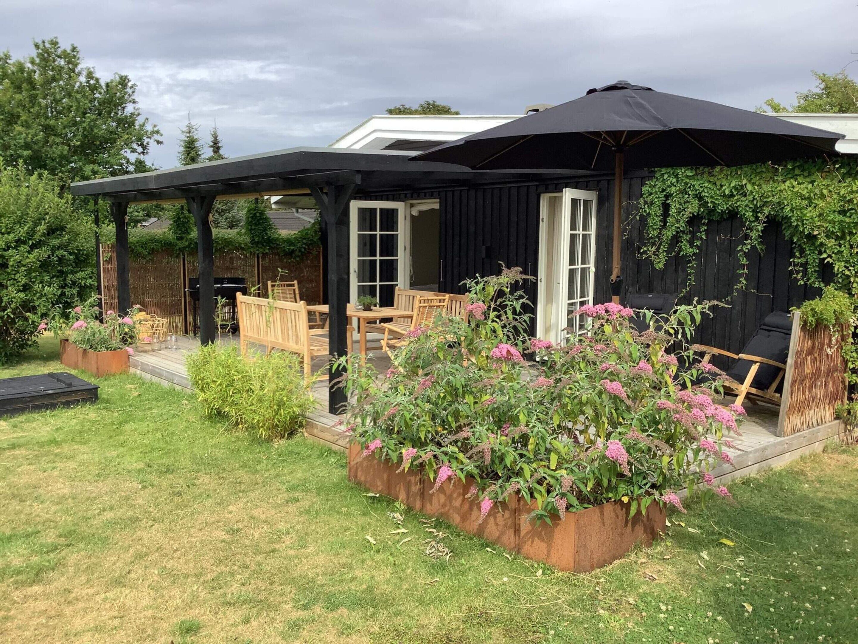 A covered patio with outdoor furniture, a garden with flowering plants, and a wooden deck.