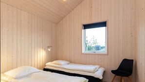 Ein Zimmer mit zwei Betten, einem Fenster, einem Sessel und einer Wandleuchte.