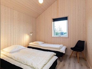 Una habitación con dos camas, una ventana, una silla y una lámpara en la pared.