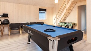 Ein Billardtisch mit blauer Spielvliesfläche und Schussstock, umgeben von Stühlen und einem kleinen Tisch mit einem Radio.