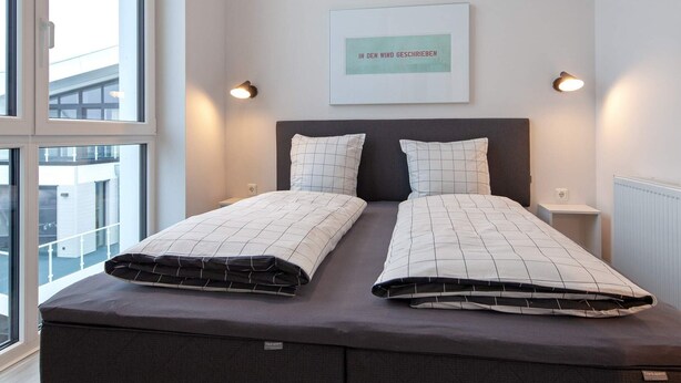 Une chambre à coucher moderne, avec un lit, deux tables de chevet, une lampe fixée au mur et une fenêtre.