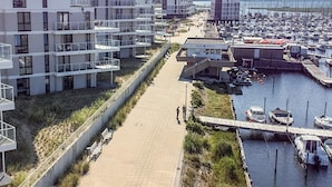 Un port de plaisance avec des bateaux, une promenade et des bâtiments modernes dotés de balcons.