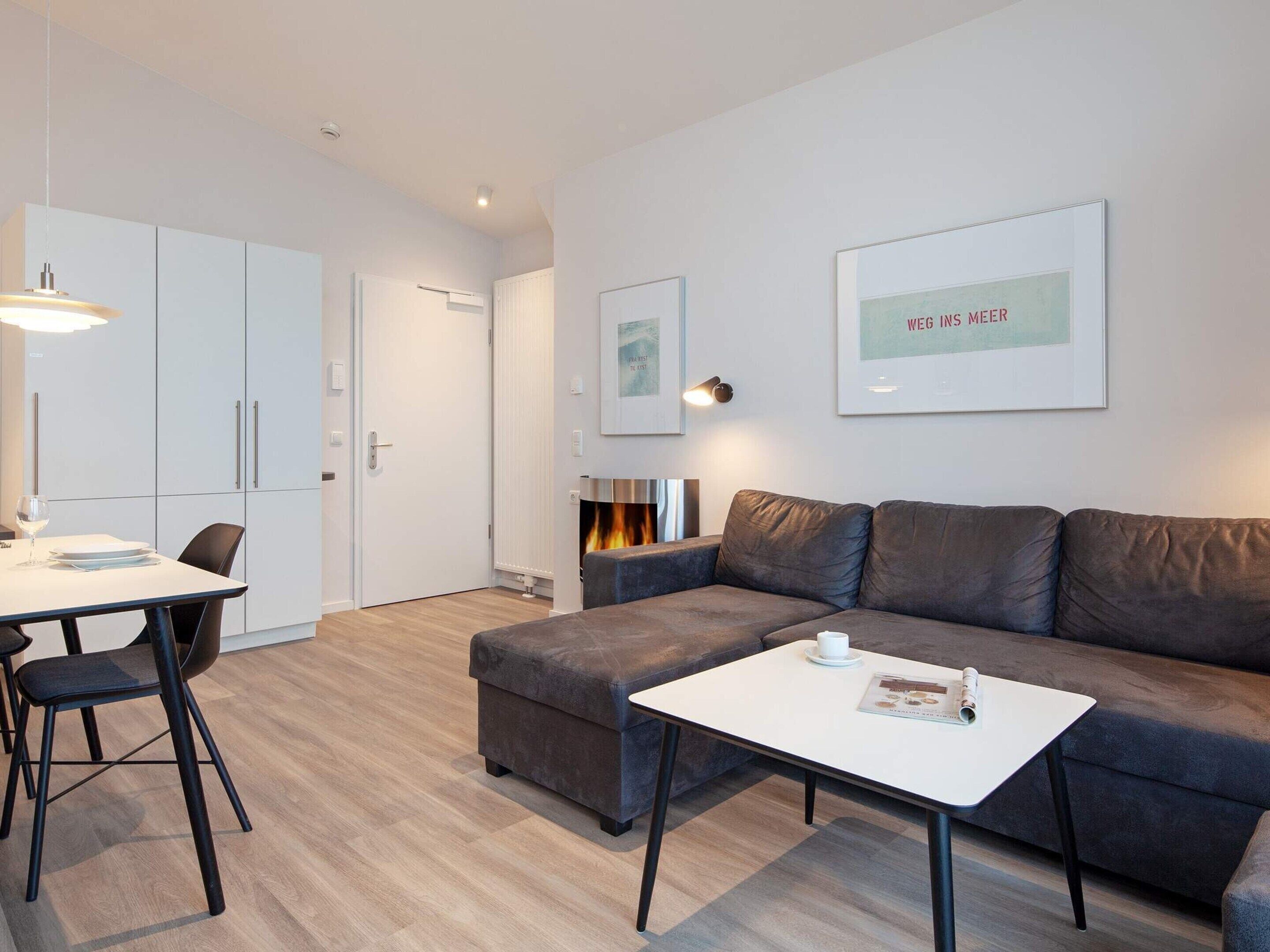 A modern living room with a sofa, a coffee table, a dining table with chairs, and a fireplace.