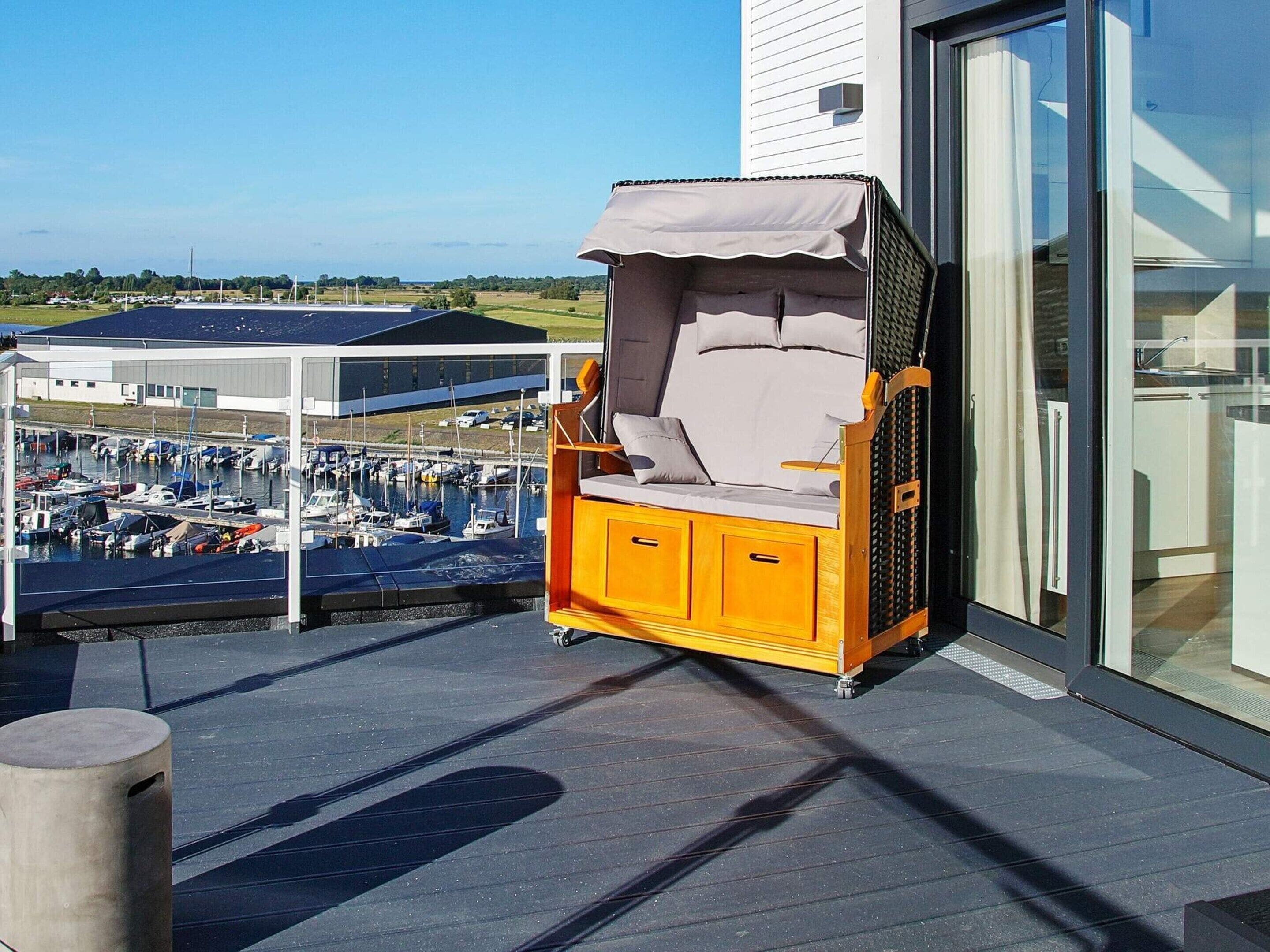 A balcony with a yellow outdoor seating area, a view of a marina, and a building with large windows.