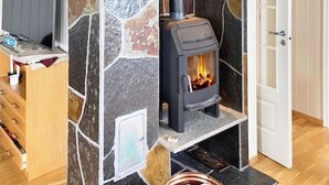 A stone fireplace with a modern stove, a television on a wooden stand, and a door to the right. - 6 Person Holiday Home in Hernar (Oygarden)