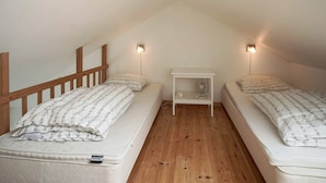 Un pequeño dormitorio en el ático con dos camas individuales, una mesita de noche con un ventilador y dos luces fijadas a la pared.