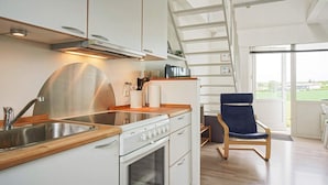 Una cocina moderna con estufa, lavamanos y encimera de madera. Se observa una silla y una escalera que da a un balcón.
