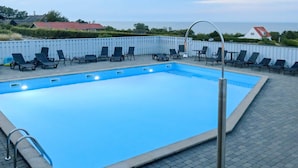 Una piscina rectangular con una reja de seguridad metálica, rodeada de sillas de descanso y una cerca blanca.