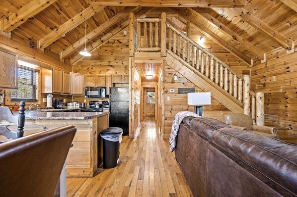 A log cabin interior with a kitchen, dining area, and a staircase leading to an upper level.