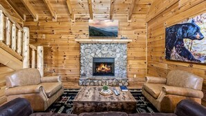A cozy cabin interior with a stone fireplace, leather sofas, and a bear painting on the wall.