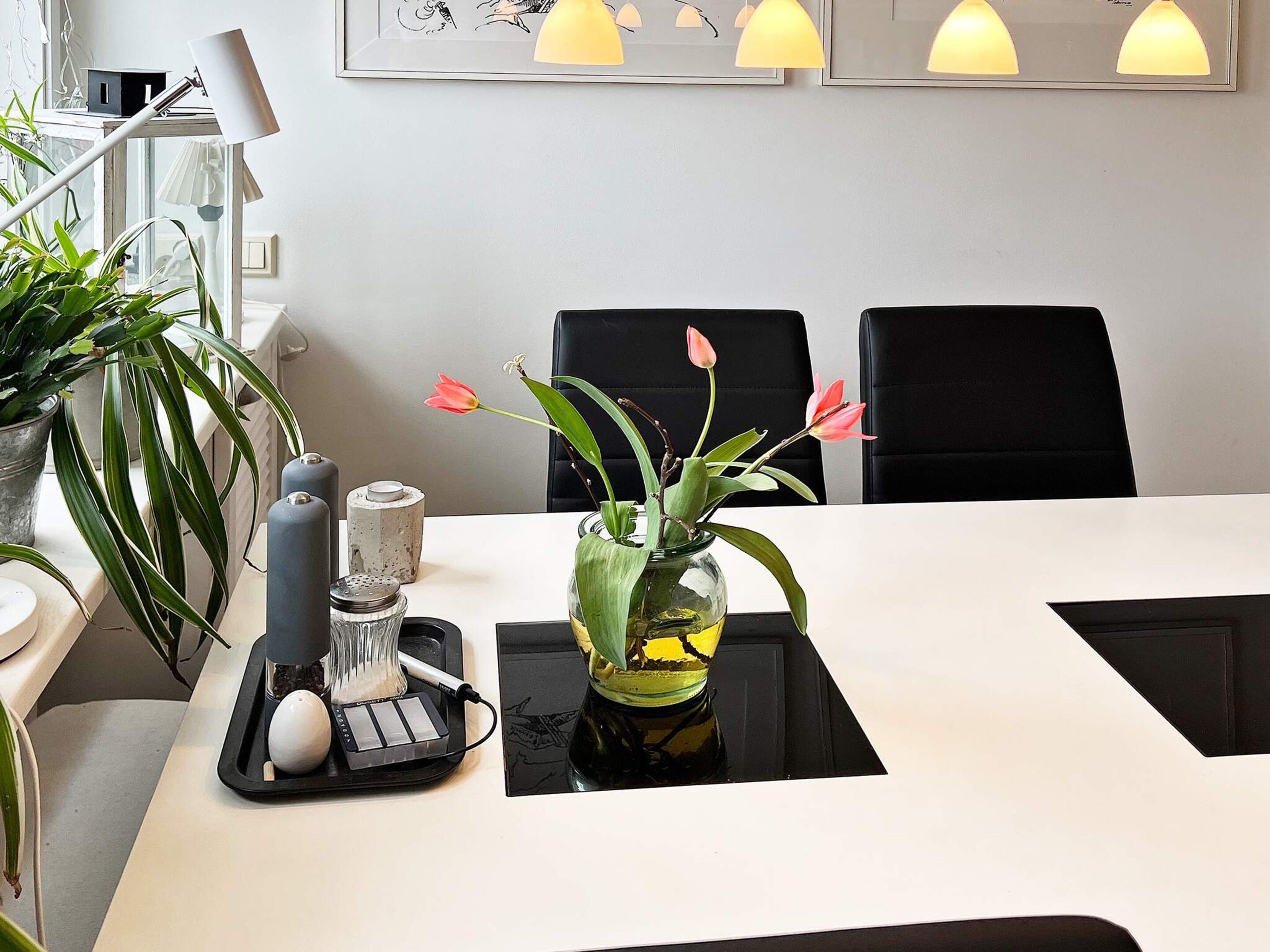 A dining table with a vase of flowers, a salt and pepper set, and a black tray with a white object.