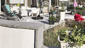 A covered outdoor seating area with lounge chairs, a table, and potted plants.