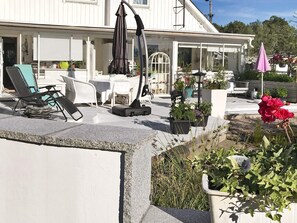 A covered outdoor seating area with lounge chairs, a table, and potted plants.