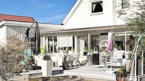 A white building with a covered patio area, outdoor seating, and potted plants.