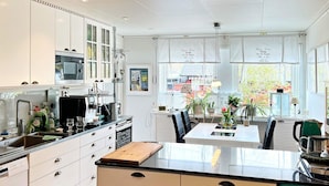 A modern kitchen with white cabinetry, a central island, and a dining area with a view of the outside. - 4 Star Holiday Home in Varmdo (Värmdö)