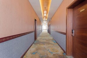 Pasillo de hotel con puertas a ambos lados, alfombra estampada y una puerta de madera a la derecha.