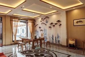 Eine Hotelhalle mit Marmorboden, einem Holzerrezeptionstresen und einer Wand mit dekorativen Wandbildern.