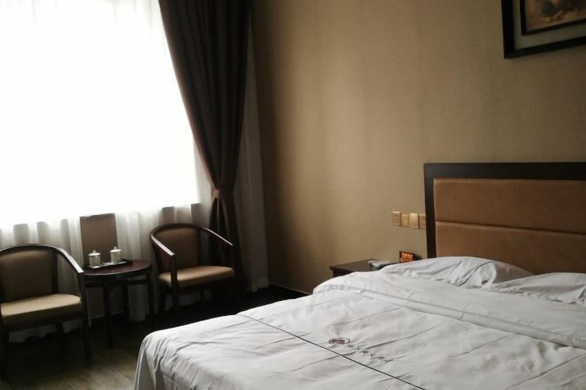A hotel room with a bed, two chairs, a small table, and a nightstand.