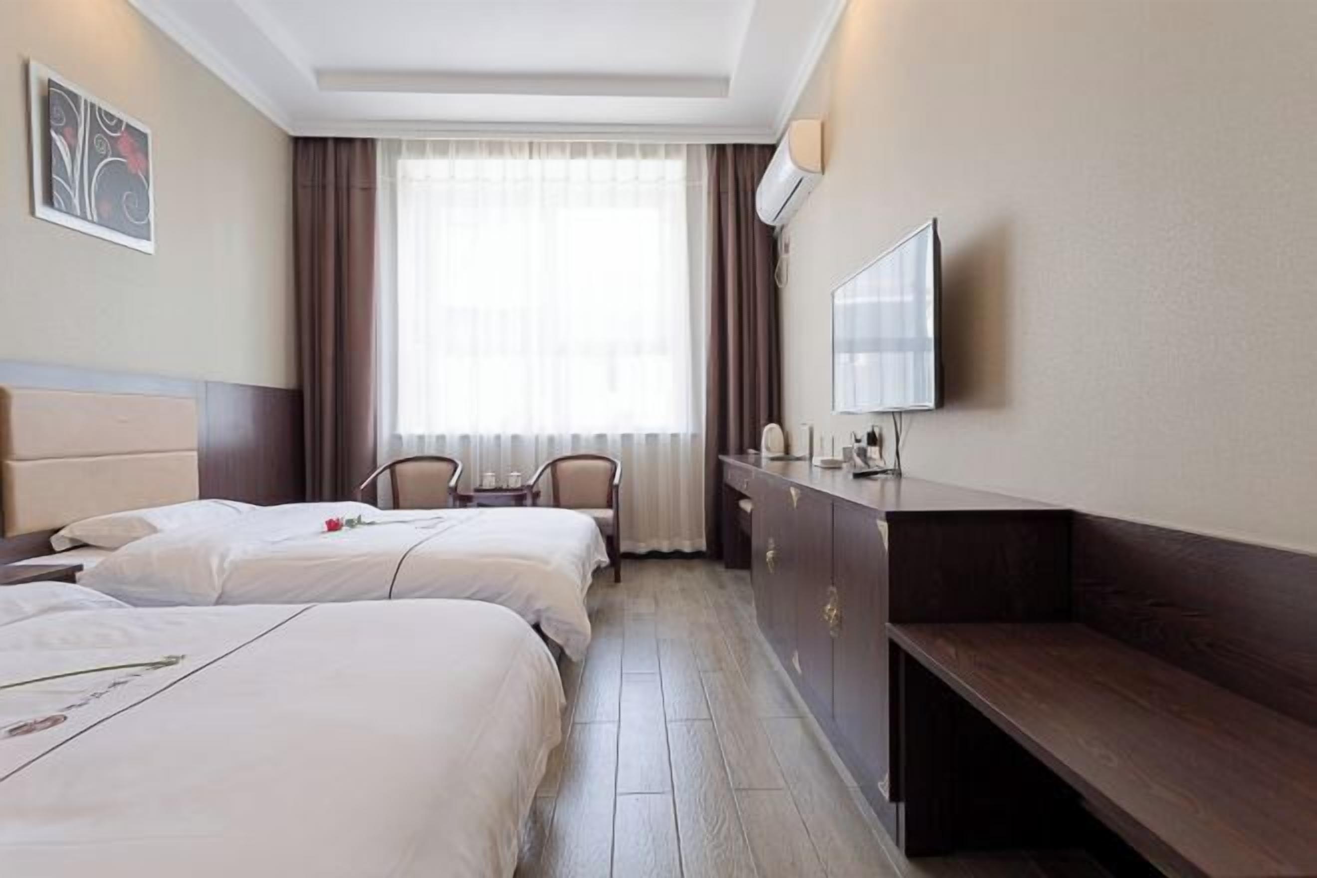 A hotel room with two beds, a desk, a chair, a TV, and a window with curtains.