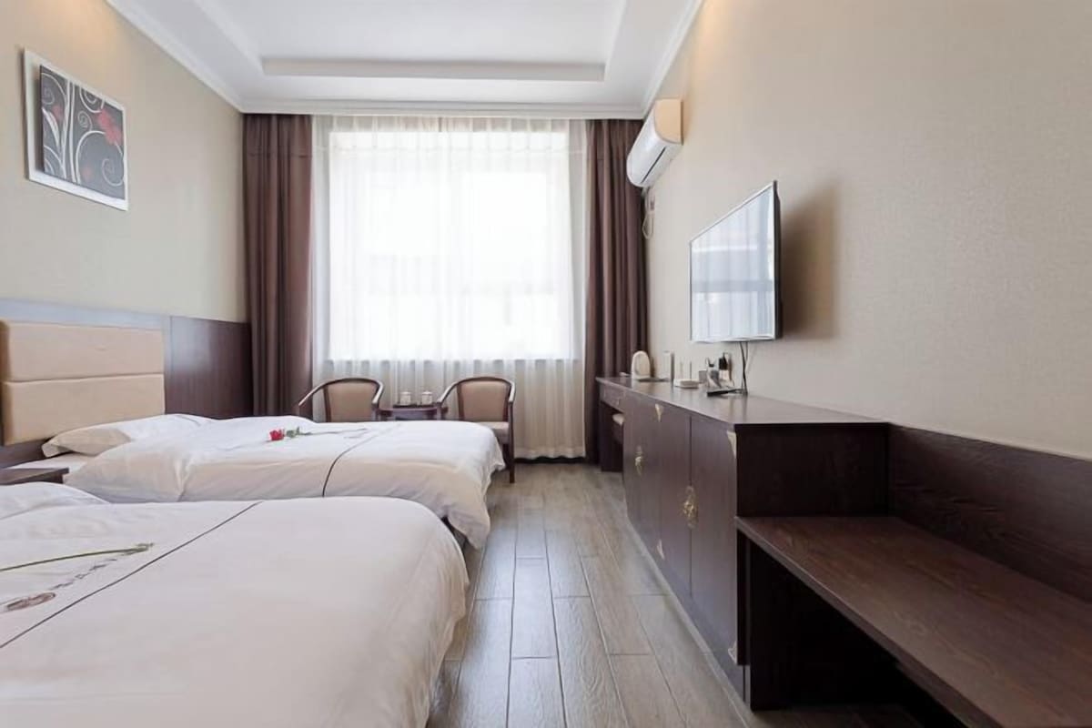 A hotel room with two beds, a desk, a chair, a TV, and a window with curtains.