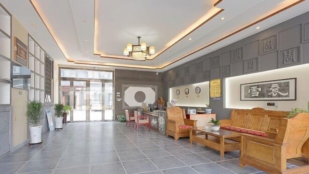 En rummelig lobby med et moderne design, der indeholder en reception, et siddeområde med møbler i træ og en lysekrone.