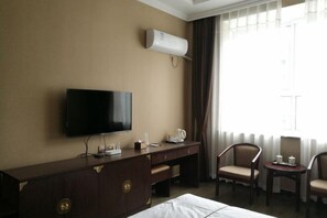 A hotel room with a flat-screen TV, a wooden dresser, a desk, two chairs, and a window with curtains. - Linjianglou Hotel (Mian County)
