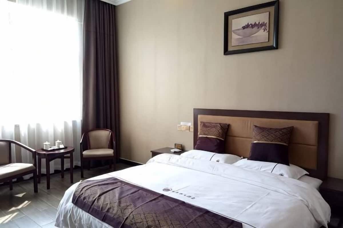 A hotel room with a large bed, a chair, a small table, and a nightstand.