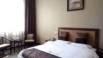 A hotel room with a large bed, a chair, a small table, and a nightstand.