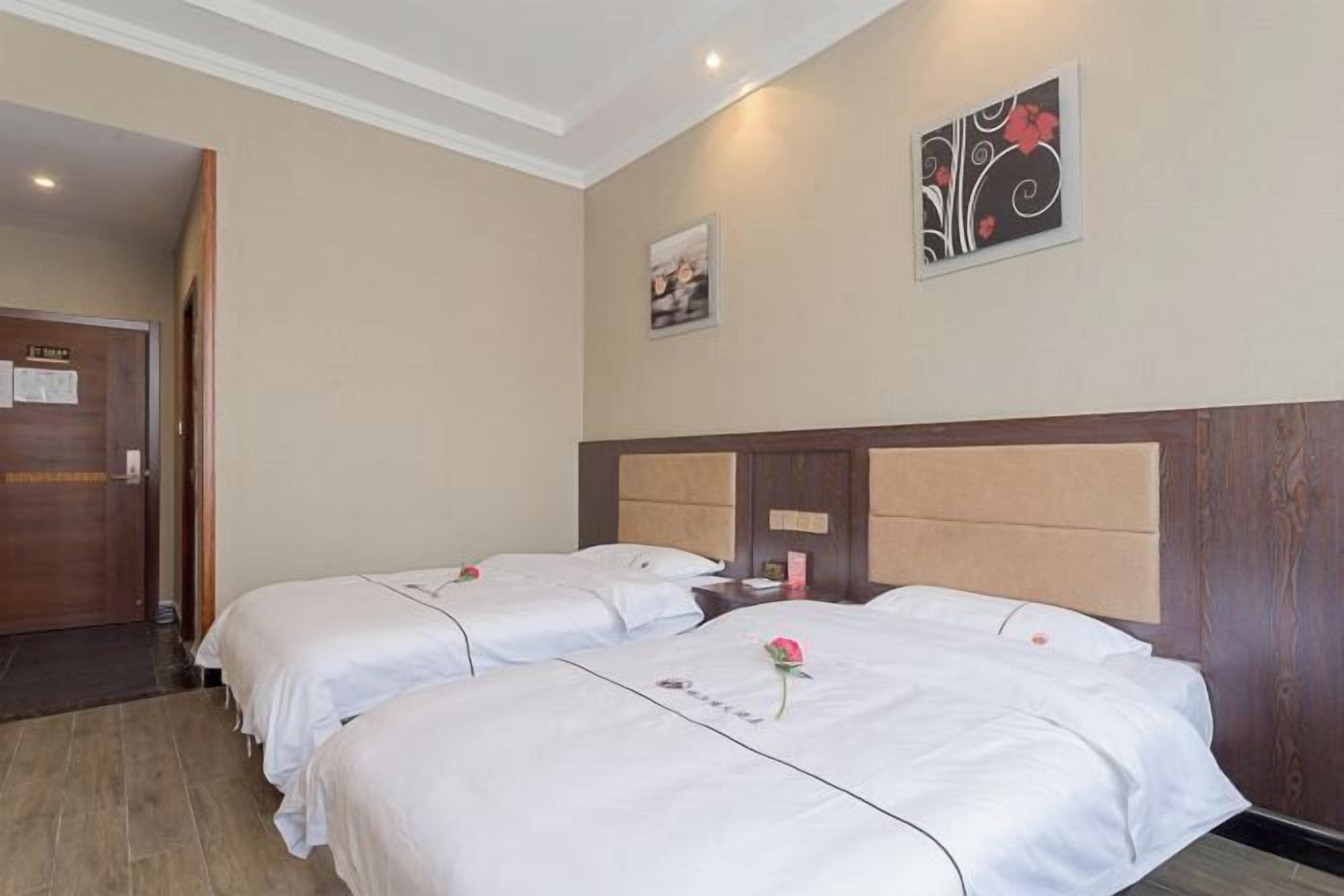 Een hotelkamer met twee bedden, een houten hoofdbord, een deur en een muur met een ingelijst schilderij en een bloemistisch ontwerp.