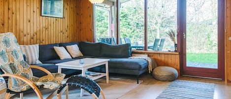 Una habitación acogedora con techo de madera, un sofá, una mesa de centro, una silla y un ventanal con vistas a zonas verdes.