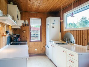 Pieni, käytännöllinen keittiö, jonka seinät ovat puuta, ja jossa on jääkaappi, pesuallas ja ikkuna, jossa on sälekaihtimet.