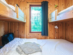 Una habitación tipo cabaña de madera con literas, una ventana con cortinas y una cama con colcha y manta.