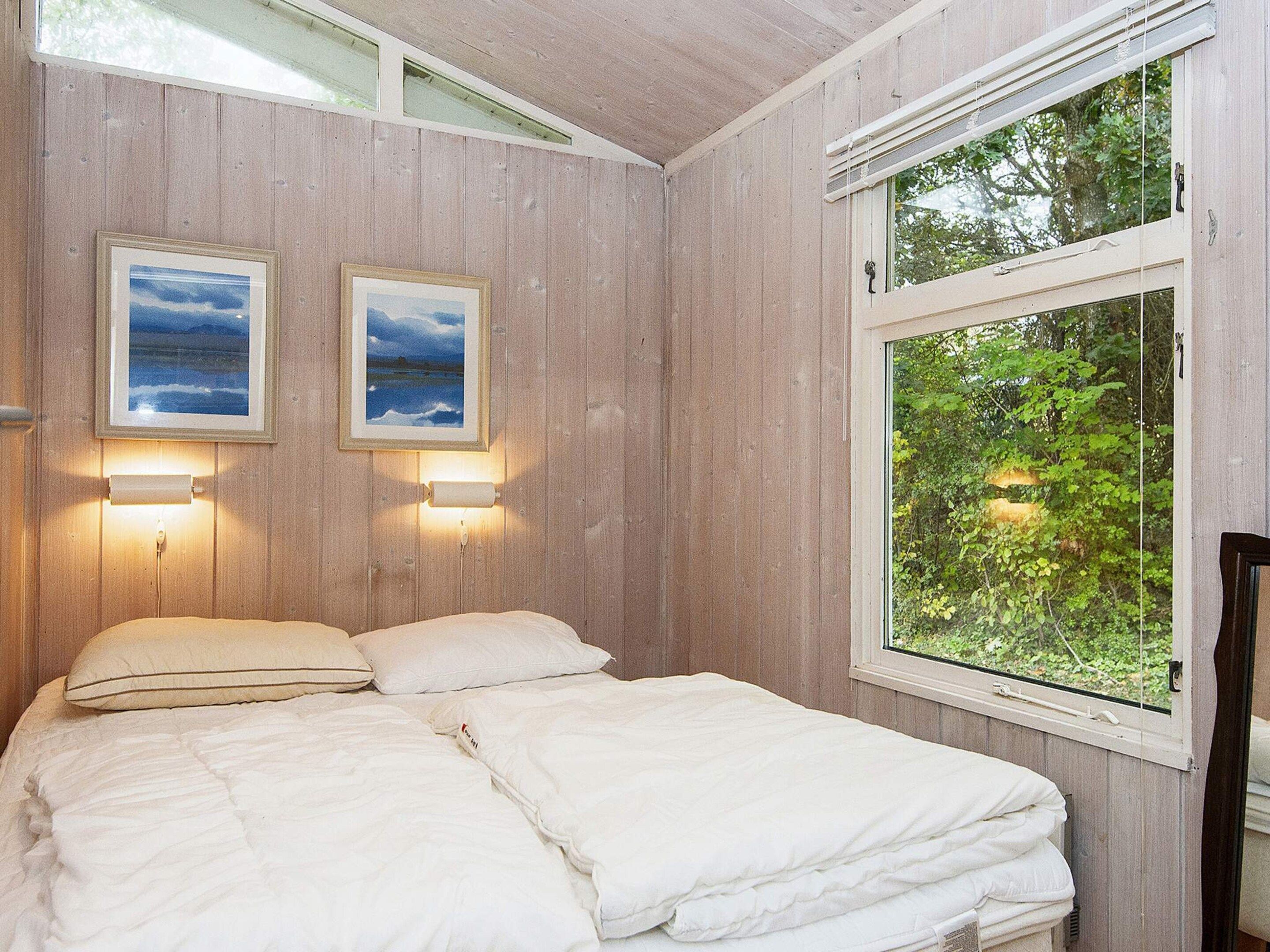 A bedroom with a bed, two wall-mounted lights, and a window with a view of greenery.