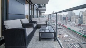 A balcony with wicker furniture and a glass table, overlooking a cityscape with buildings and a parking lot. - beauti 2 bedroom with 2 bathroom condo in downtown (Calgary)