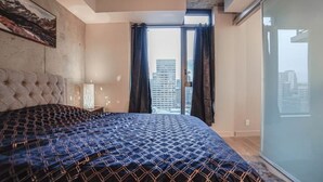 A bedroom with a large bed, a tufted headboard, a city view through a window, and a modern ceiling. - beauti 2 bedroom with 2 bathroom condo in downtown (Calgary)