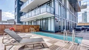 A rooftop pool area with sun loungers, a wooden deck, and a glass building in the background. - beauti 2 bedroom with 2 bathroom condo in downtown (Calgary)